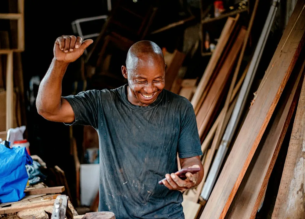 Un menuisier souriant regarde son téléphone dans son atelier